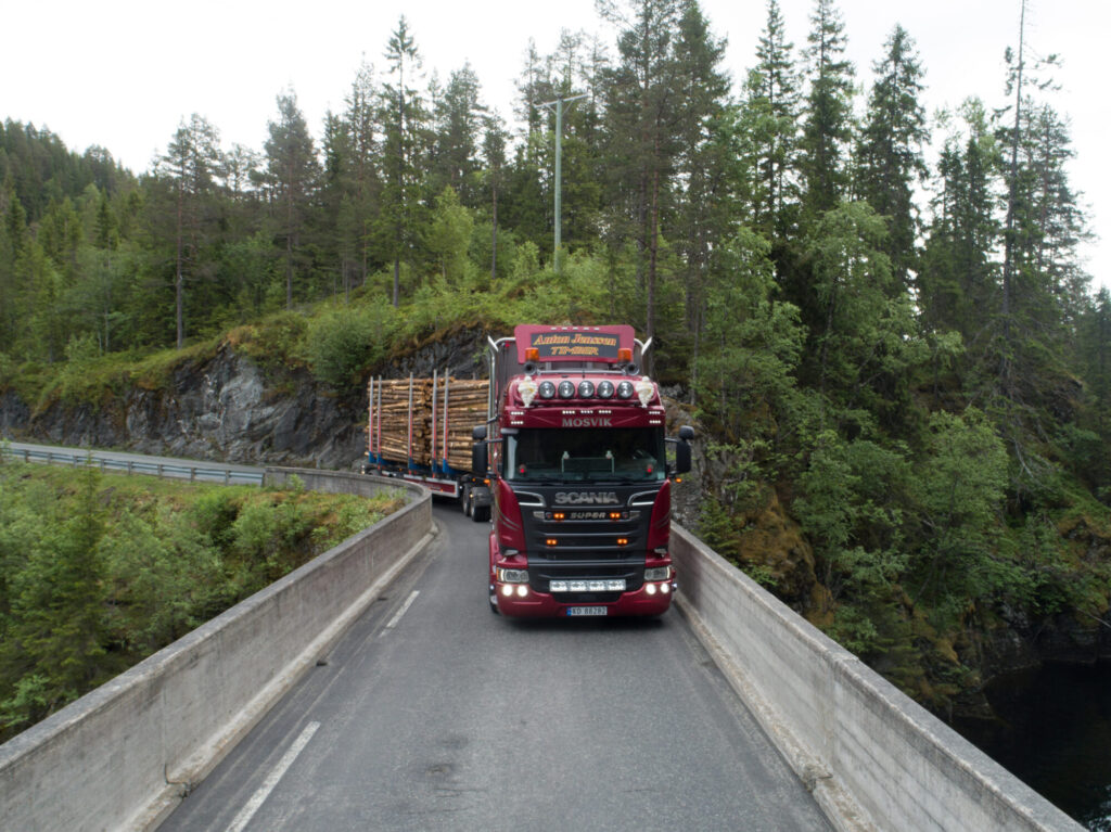 Tømmerbil med lass på vei over bru.