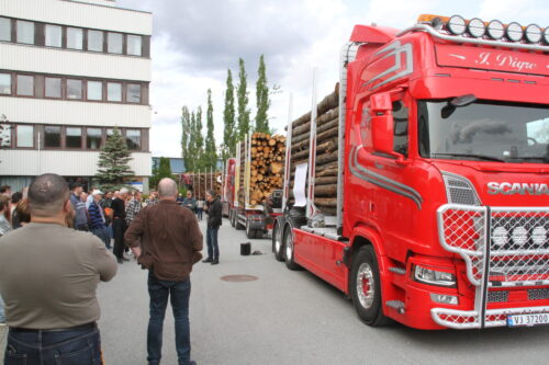Tømmerbiler med lass og mennesker som ser på.