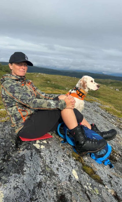 Dame sitter med fuglehund på fjellet.