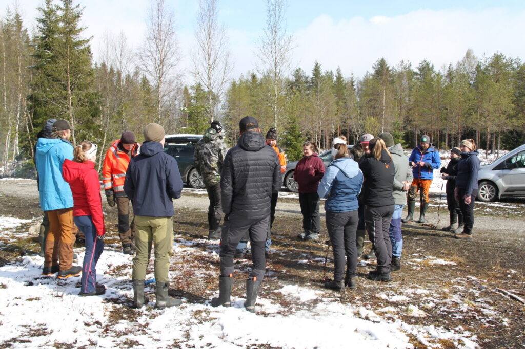 Gruppe mennesker samlet rundt bål i skogen.