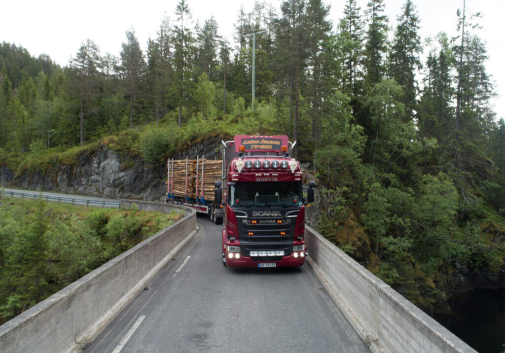 Tømmerbil med lass på vei over bru.