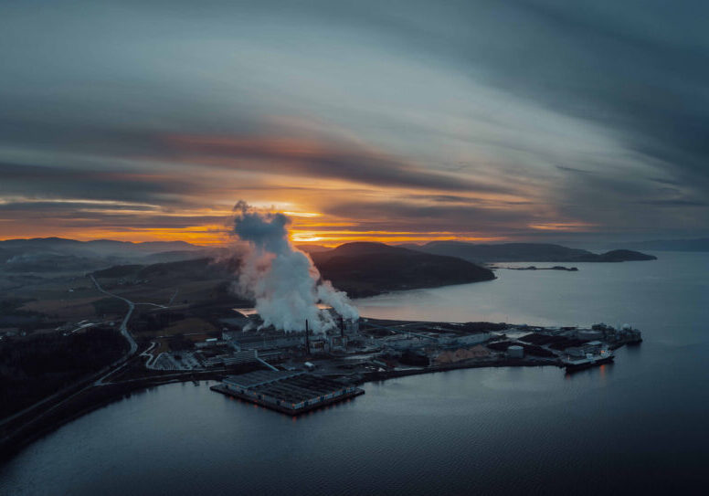 Pano norske skog_solnedgang Papirfabrikk ved fjorden om kvelden. Bilde tatt fra lufta.